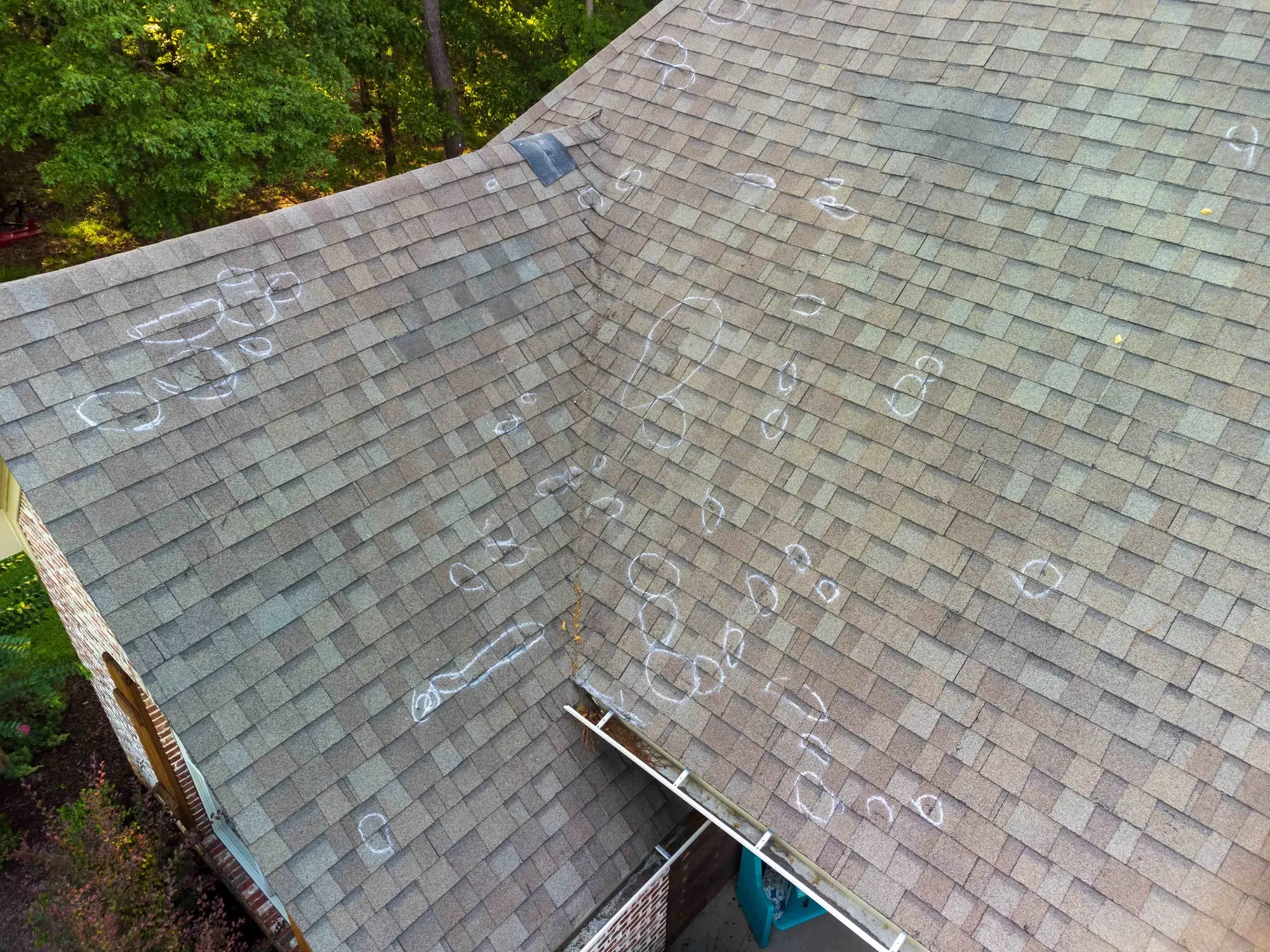 Hail impacts circled in chalk across a shingle roof during claim documentation